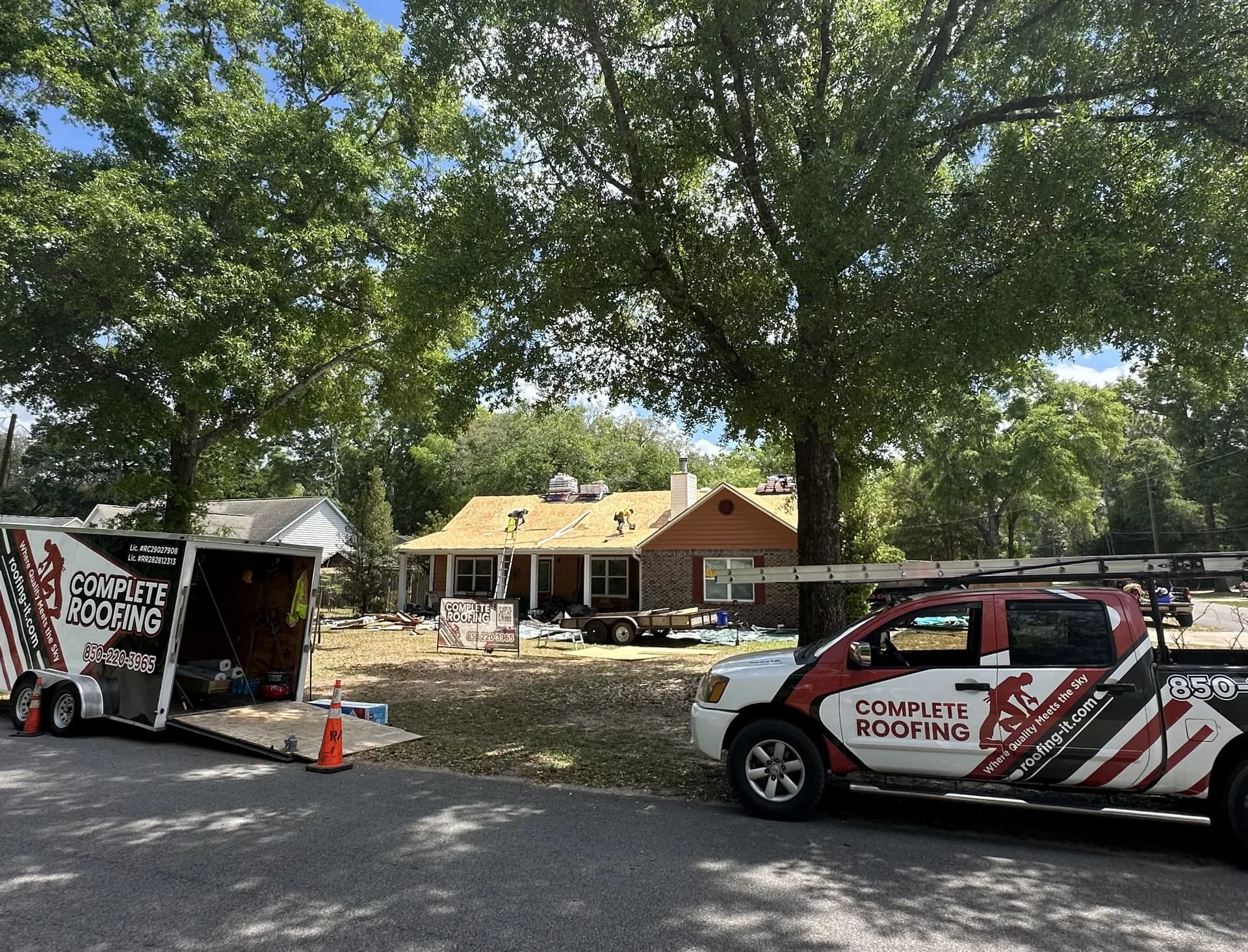 Complete Roofing LLC crew performing hurricane wind-damage repair on a Pensacola-area home with the company truck and trailer on site